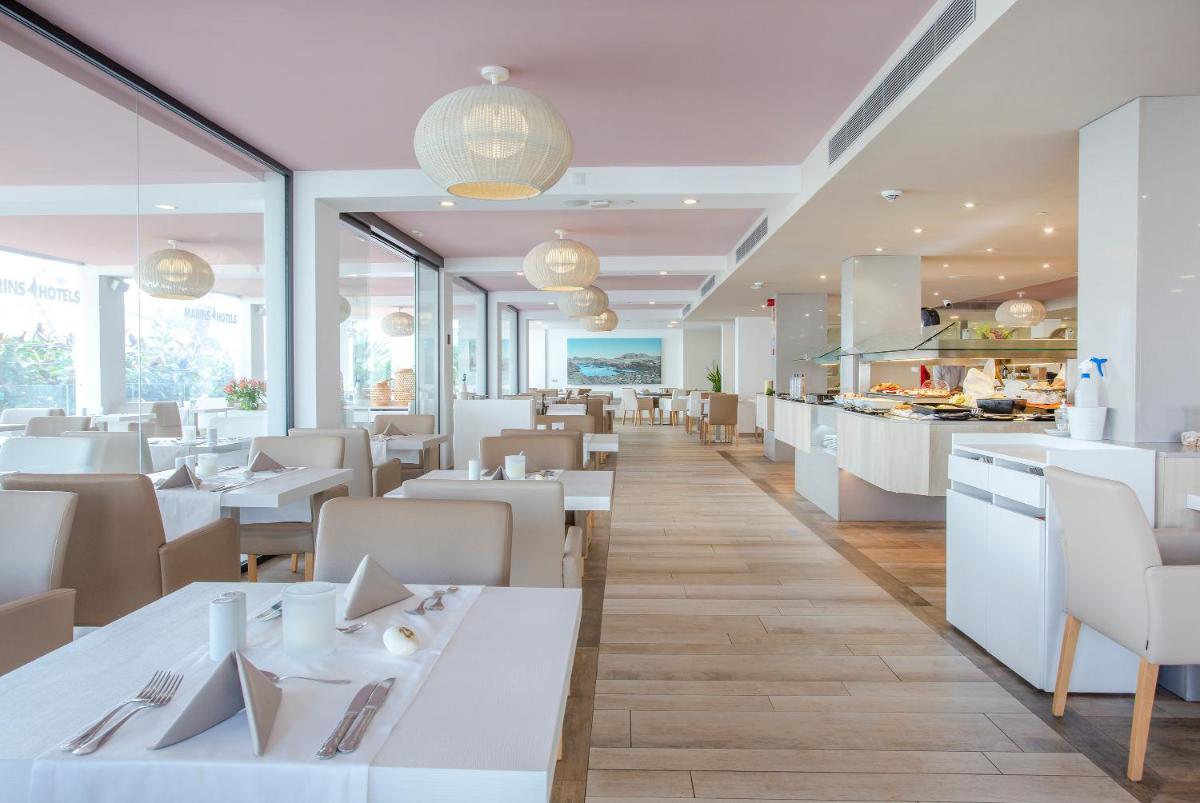 Un restaurante con mesas y sillas blancas y una cocina. en Marins Playa, en Cala Millor