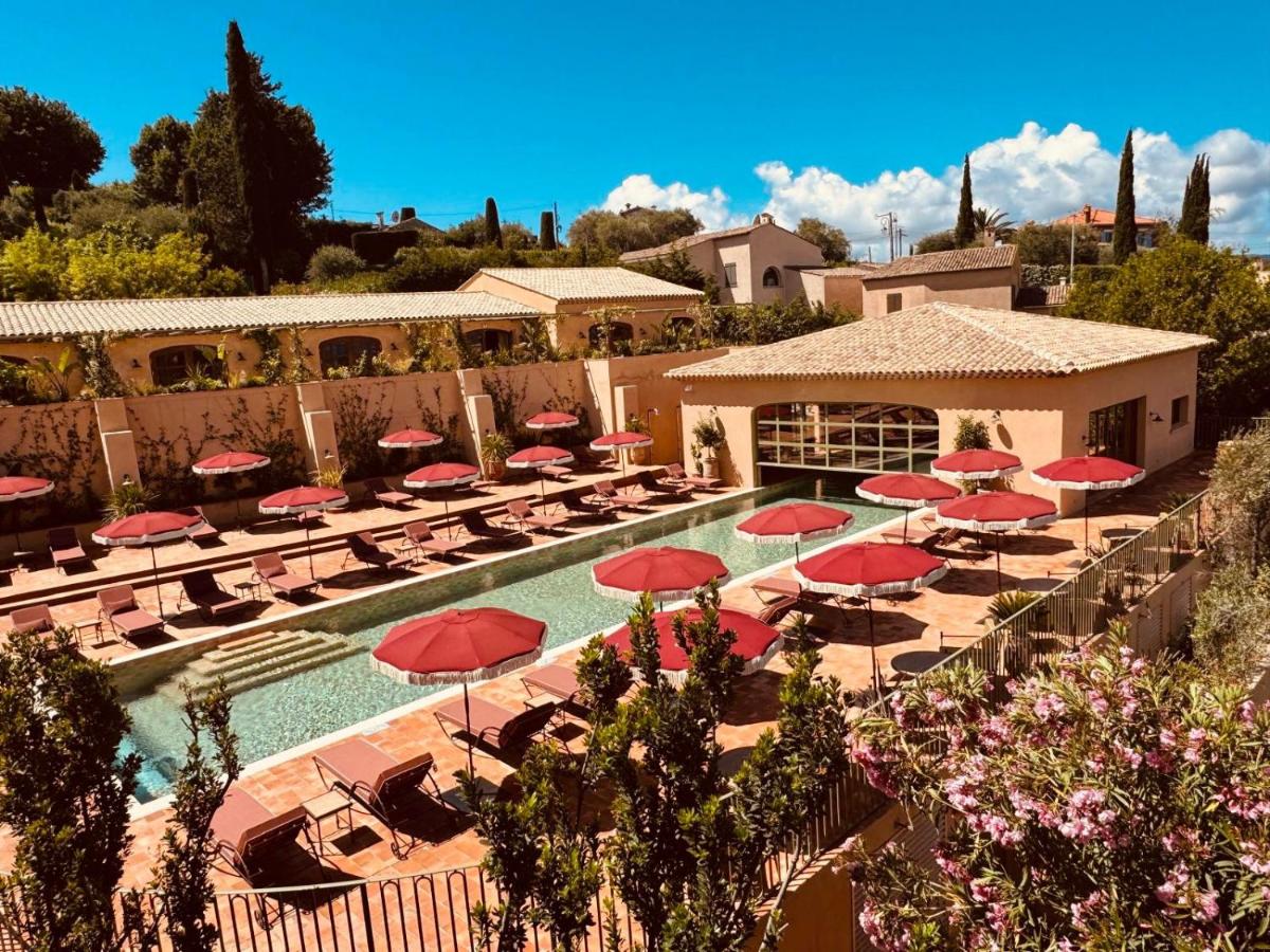 une piscine avec des parasols rouges et des chaises longues dans l'établissement Le Mas Candille, à Mougins