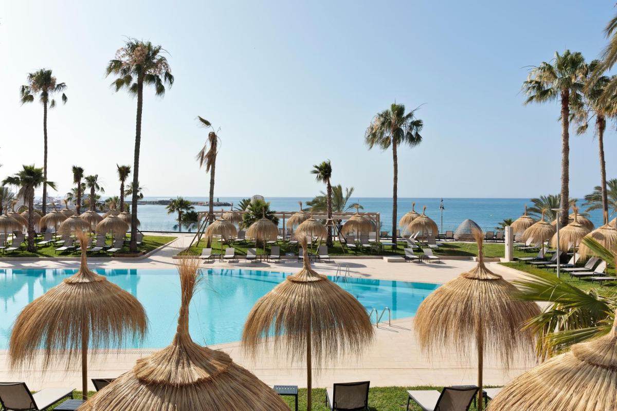 Una piscina tipo resort con sombrillas de paja y palmeras. en Hotel Best Triton, en Benalmádena