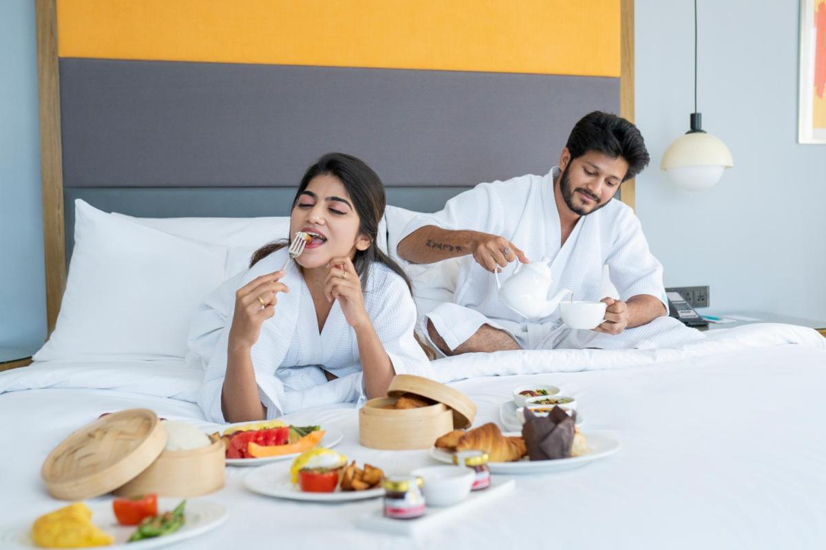 a man and woman sitting in bed eating food at Le Meridien Hyderabad in Hyderabad