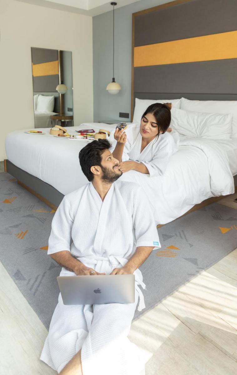 a man and woman sitting on a bed with a laptop at Le Meridien Hyderabad in Hyderabad