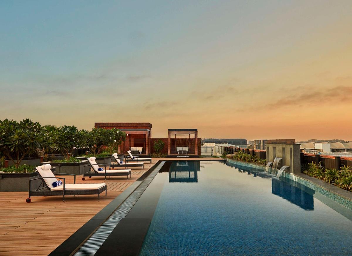 a pool on the roof of a building with lounge chairs at Doubletree By Hilton Bengaluru Whitefield in Bengaluru