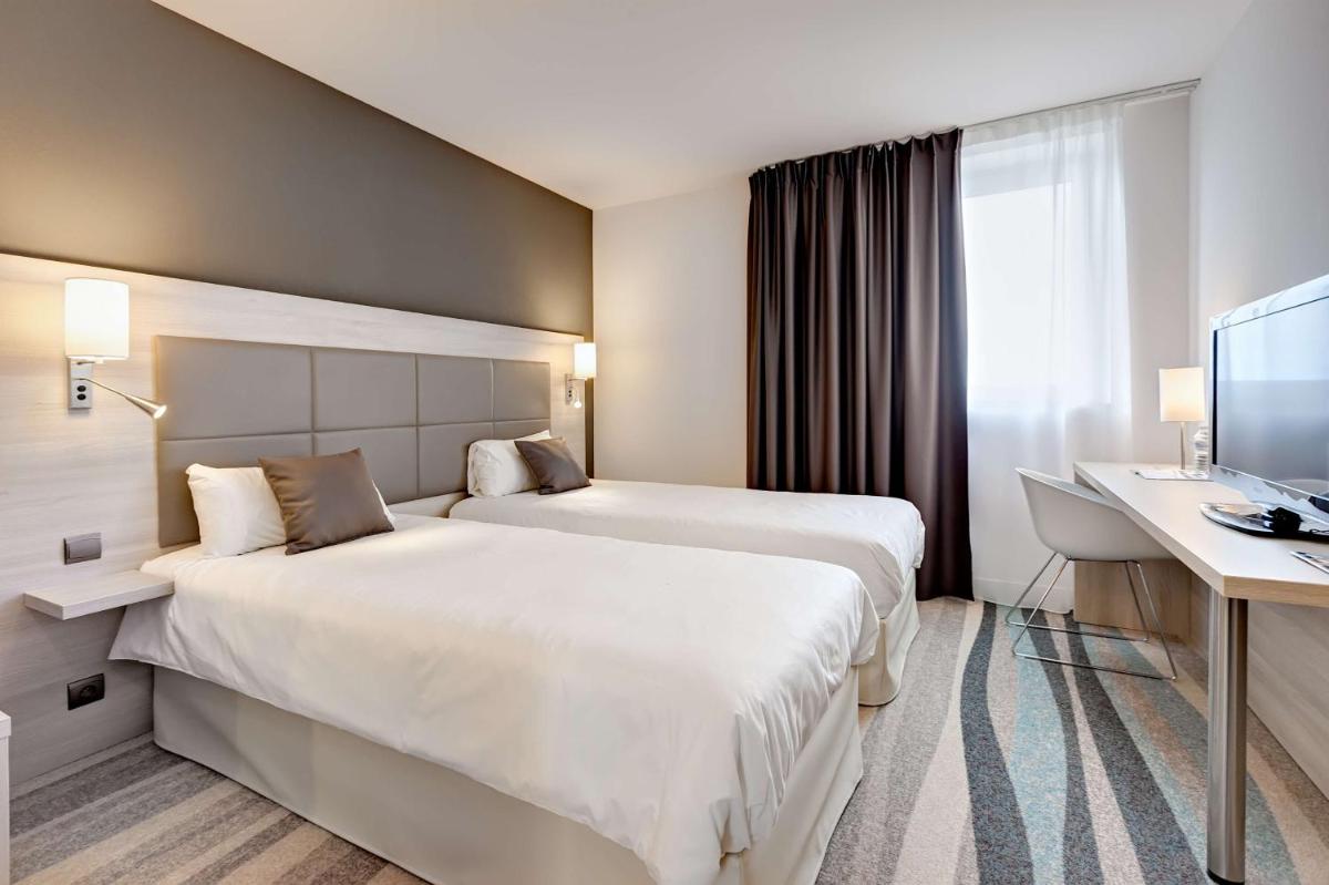 une chambre d'hôtel avec deux lits et un bureau dans l'établissement Brit Hotel Vendée Mer, à La Mothe-Achard