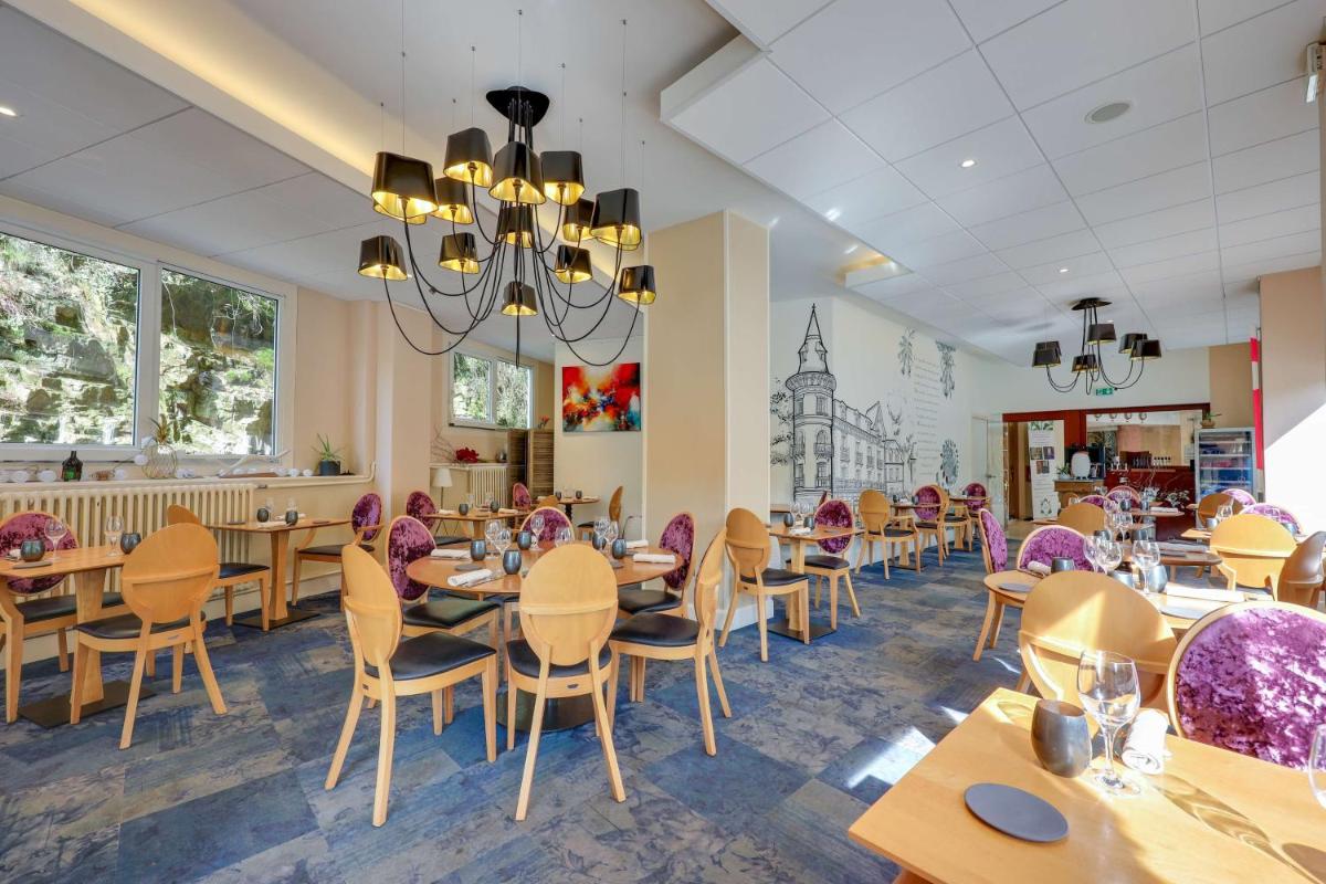 un restaurant avec des tables, des chaises et un lustre dans l'établissement BRIT HOTEL & SPA Le Roc au Chien, à Bagnoles-de-l'Orne