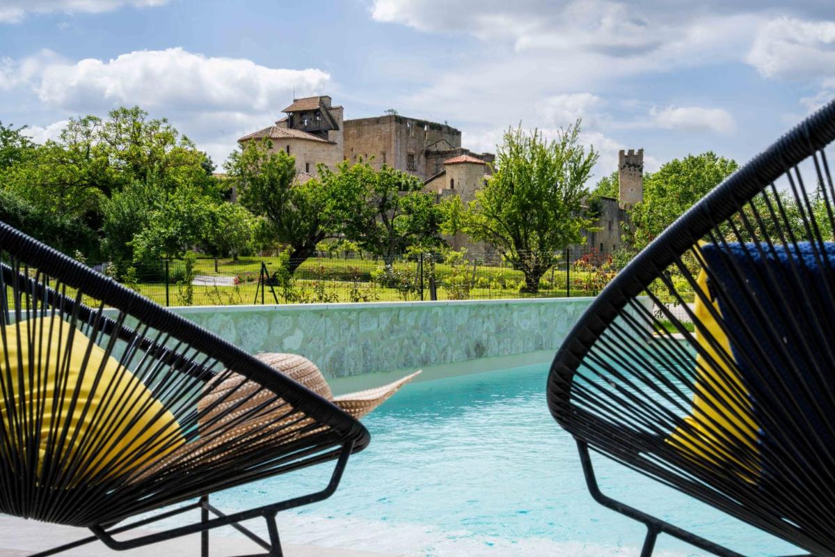 deux chaises assises à côté d'une piscine avec un château dans l'établissement Logis L'Auberge de Larressingle, à Larressingle
