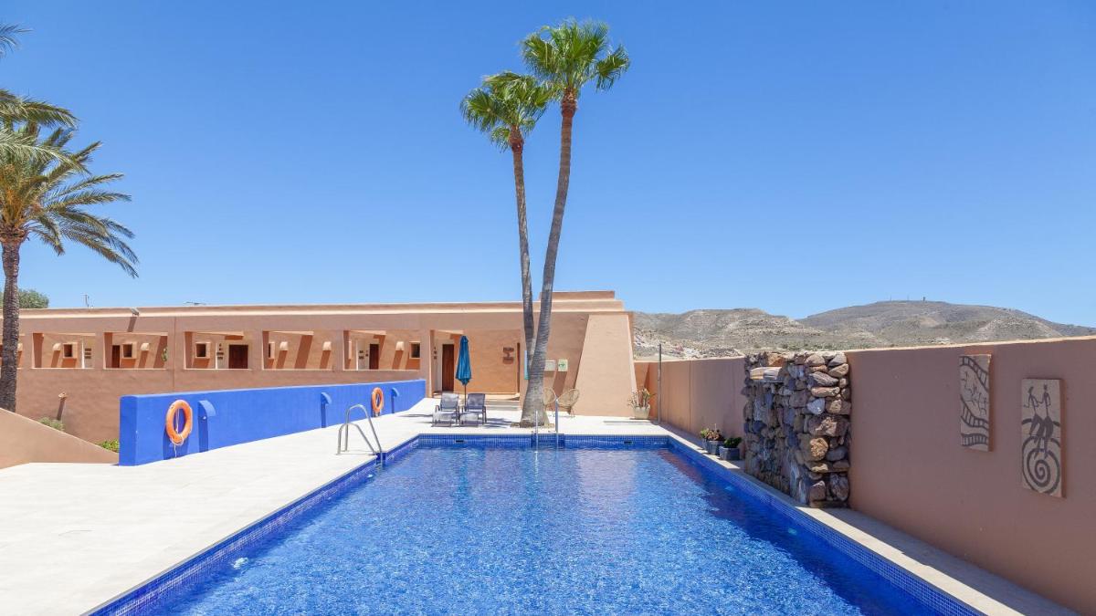 Una piscina en un resort con palmeras y un edificio. en Hotel de Naturaleza Rodalquilar & Spa Cabo de Gata, en Rodalquilar