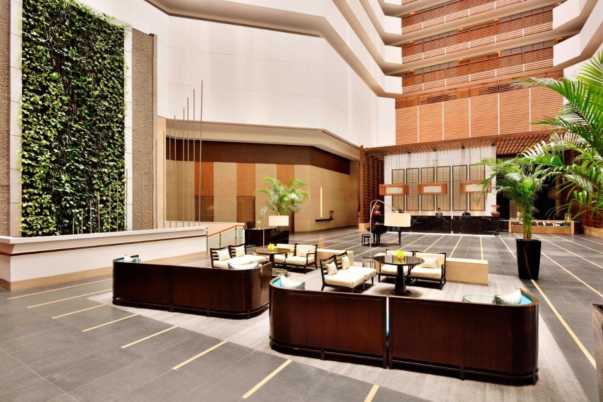 a lobby with tables and chairs in a building at The Westin Hyderabad Mindspace in Hyderabad