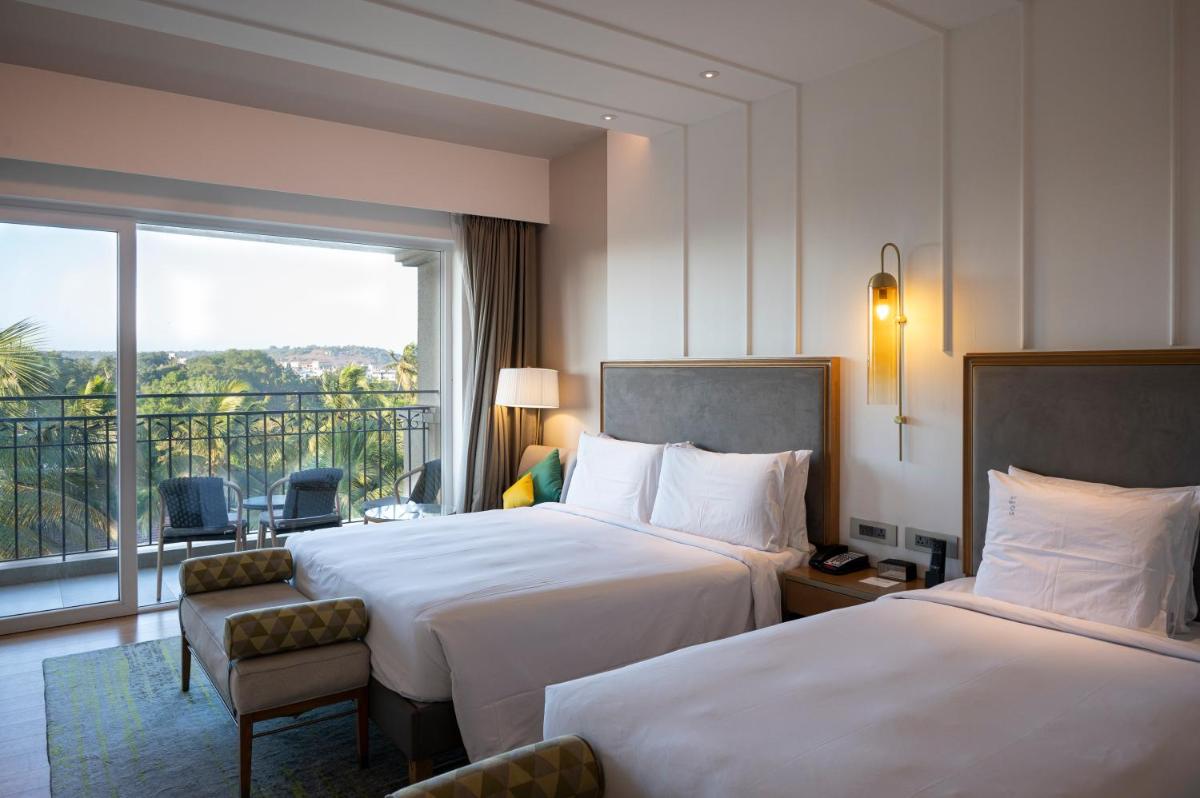 a hotel room with two beds and a balcony at Holiday Inn Goa Candolim in Candolim a hotel room with two beds and a balcony at Holiday Inn Goa Candolim in Candolim