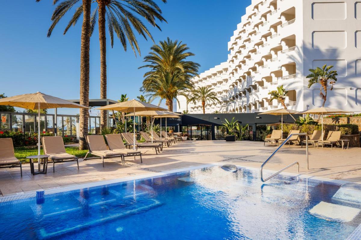 Una piscina con sillas y sombrillas al lado de un hotel. en Hapimag San Agustín, en San Agustín