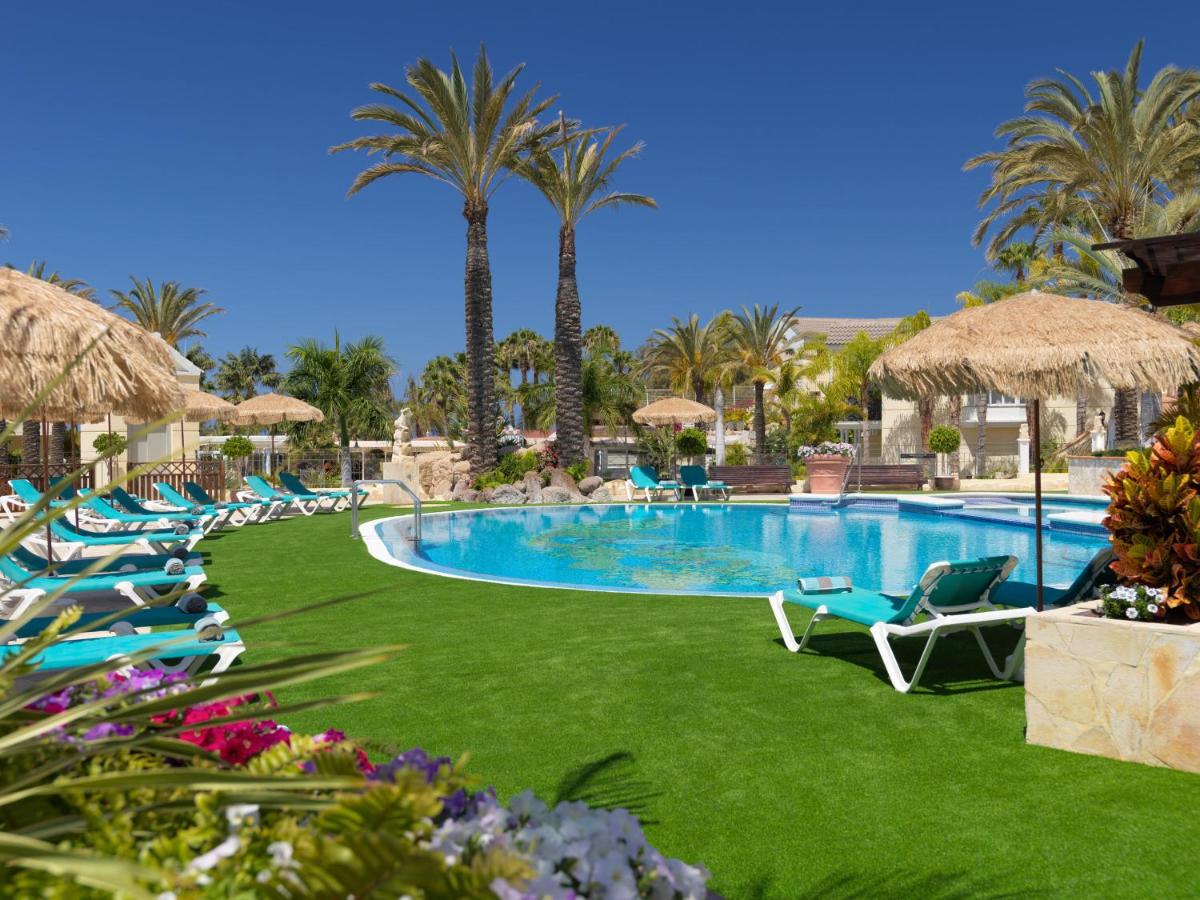 Una piscina con sillas de jardín y palmeras. en Gran Oasis Resort, en Playa de las Américas