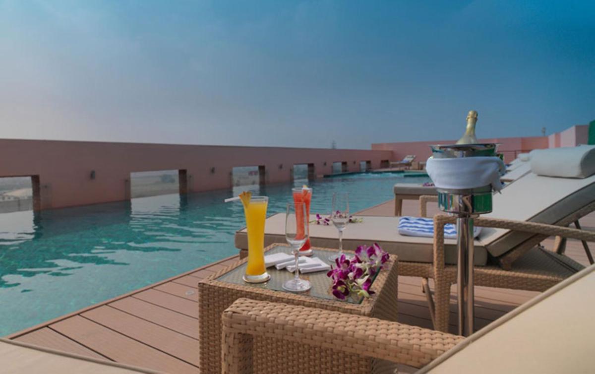 a swimming pool with a table with drinks on a deck at Hotel Royal Orchid Jaipur, Tonk Road in Jaipur