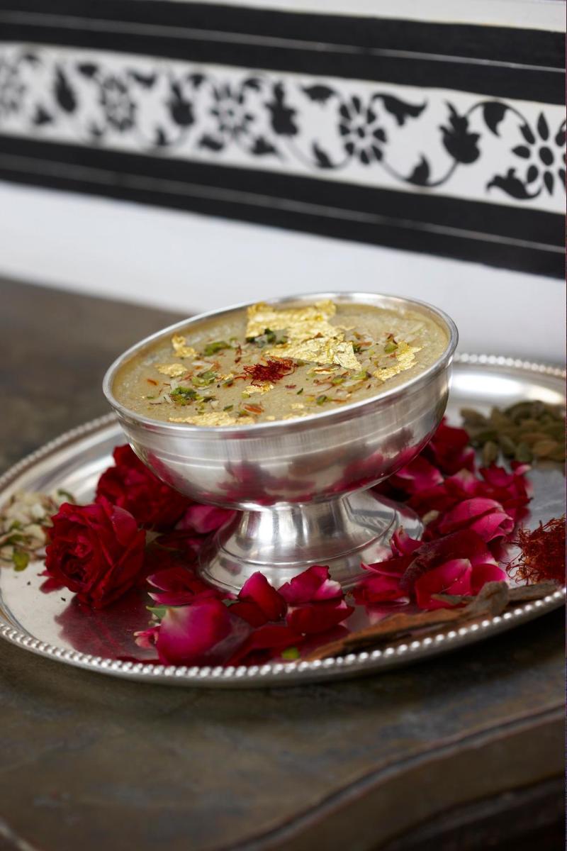 a bowl of food on a plate with red flowers at The Raj Palace (Small Luxury Hotels of the World) in Jaipur