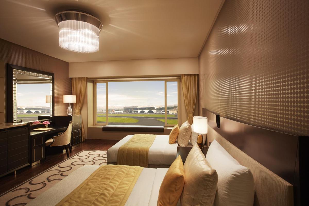 a hotel room with two beds and a desk and a window at Taj Santacruz in Mumbai