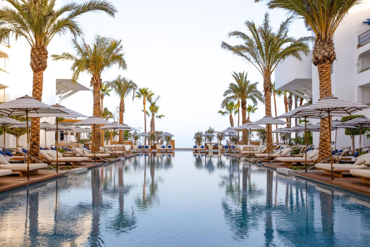 una piscina con palmeras, sillas y sombrillas en METT Marbella Estepona, en Estepona