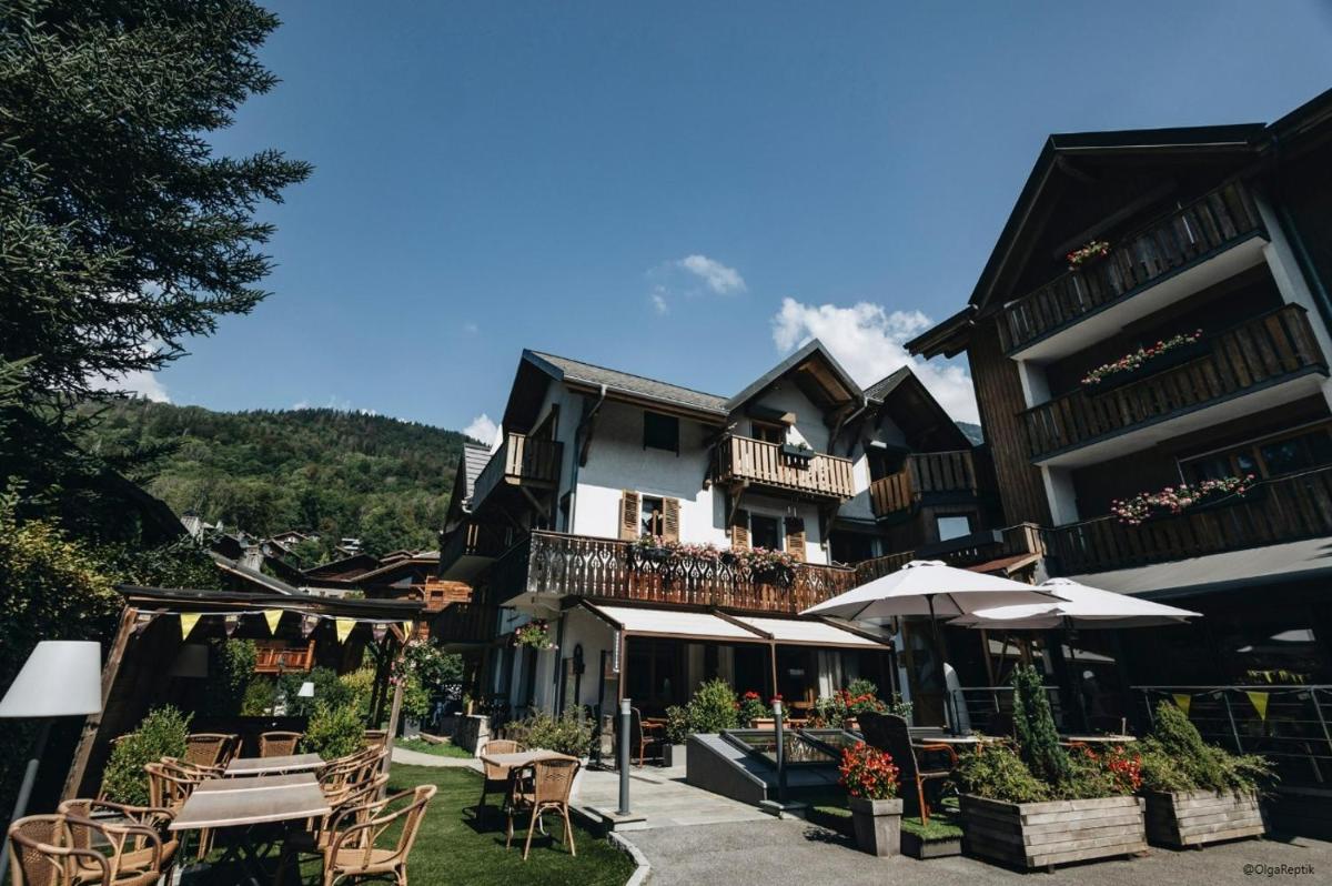 un bâtiment avec des tables et des parasols devant lui dans l'établissement Logis Hotel Gai Soleil, à Samoëns