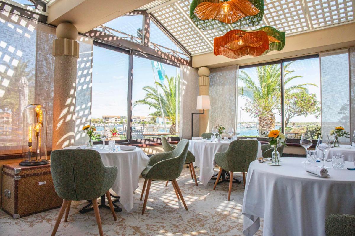 un restaurant avec des tables et des chaises blanches et des fenêtres dans l'établissement Relais et Châteaux Thalasso & Spa Ile de la Lagune, à Saint-Cyprien