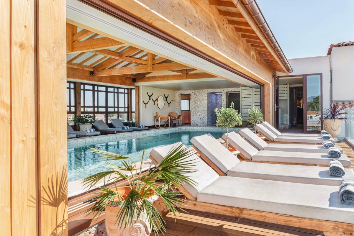 une piscine intérieure avec des chaises longues blanches et une maison dans l'établissement Relais et Châteaux Thalasso & Spa Ile de la Lagune, à Saint-Cyprien