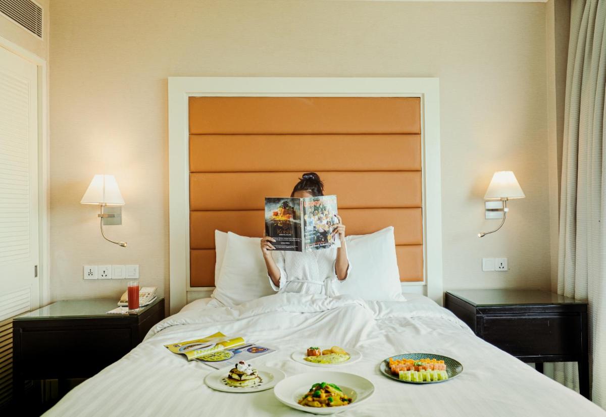 a woman sitting on a bed with two plates of food at Marriott Executive Apartment - Lakeside Chalet, Mumbai in Mumbai