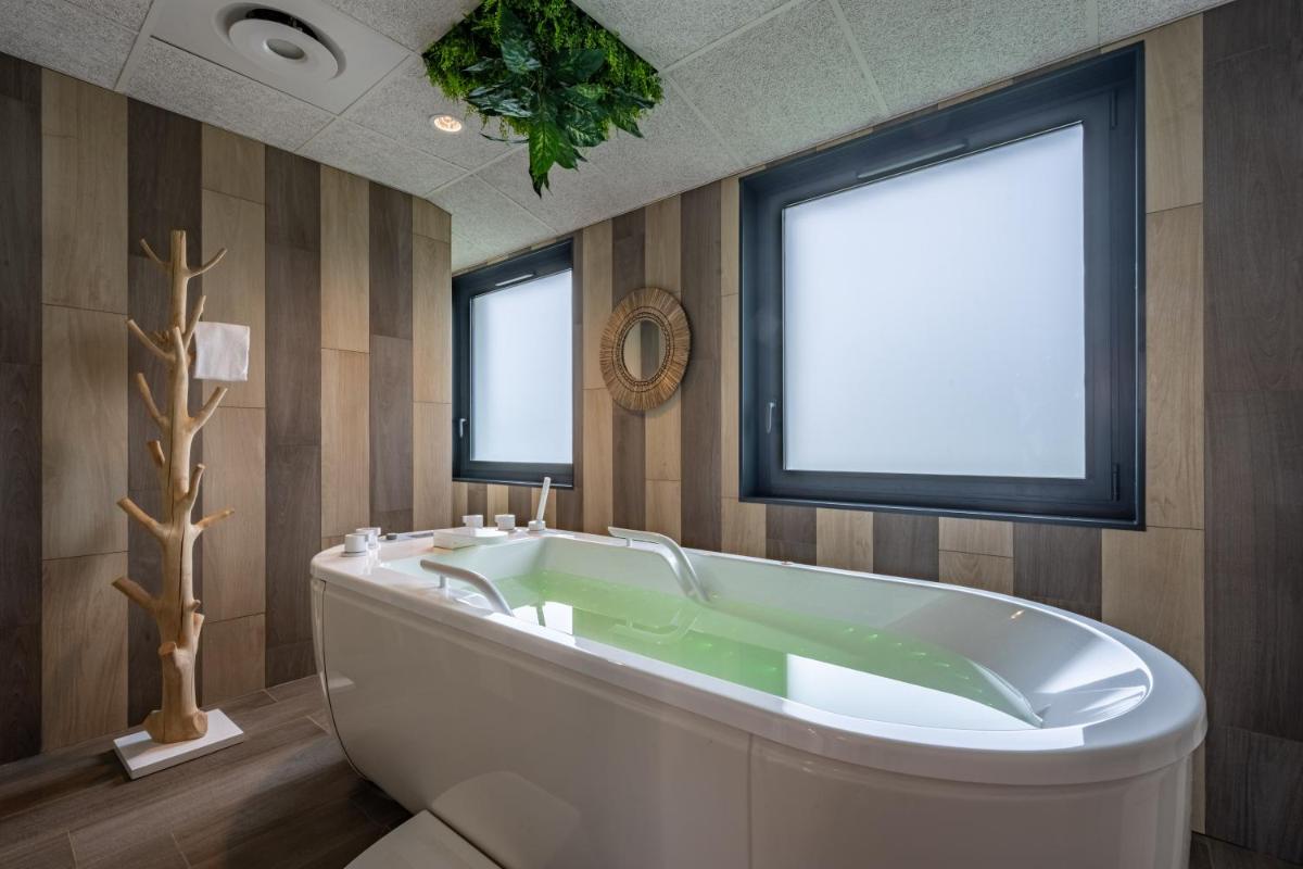 La salle de bains est pourvue d'une grande baignoire et de 2 fenêtres. dans l'établissement Hôtel Atalante - Relais Thalasso & Spa, à Sainte-Marie de Ré