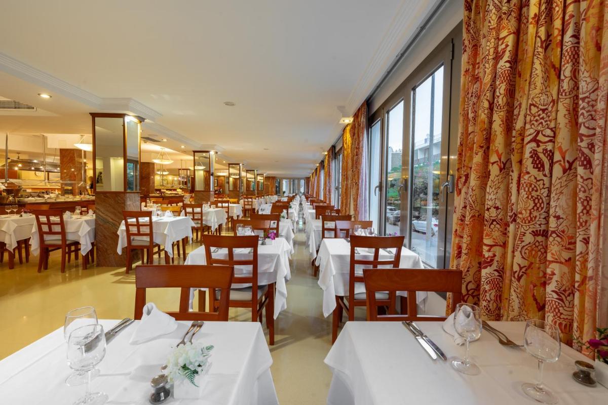 Un restaurante con mesas y sillas blancas y ventanas. en Bellamar Hotel Beach & Spa, en San Antonio