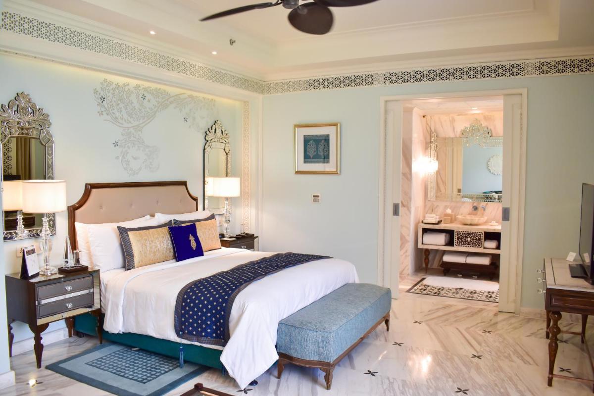 a bedroom with a large bed and a bathroom at The Leela Palace Jaipur in Jaipur