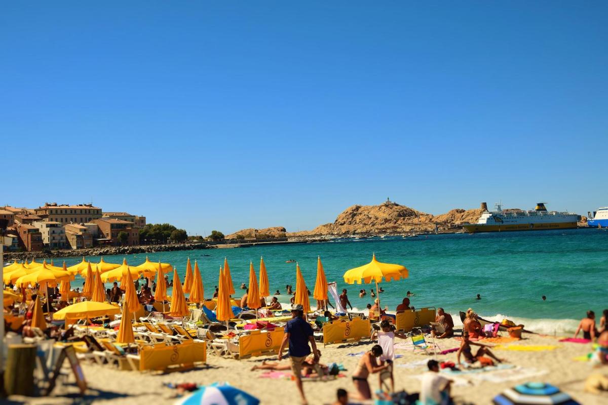 une foule de gens sur une plage avec des parasols et l'eau dans l'établissement Hôtel Liberata & Spa, à LʼÎle-Rousse