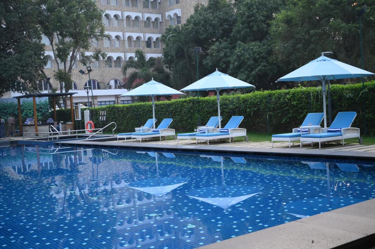 a swimming pool with lounge chairs and umbrellas at Taj Ganges Varanasi in Varanasi