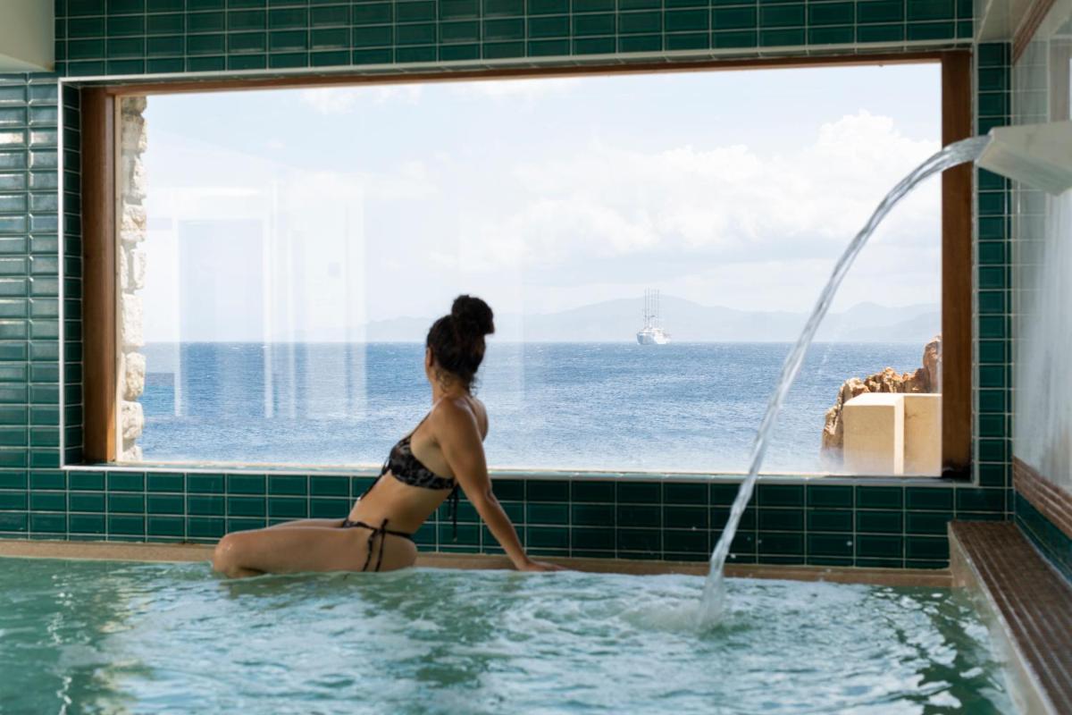 une femme dans une baignoire regardant l'océan par la fenêtre dans l'établissement Hotel La Pietra Restaurant & Spa, à LʼÎle-Rousse
