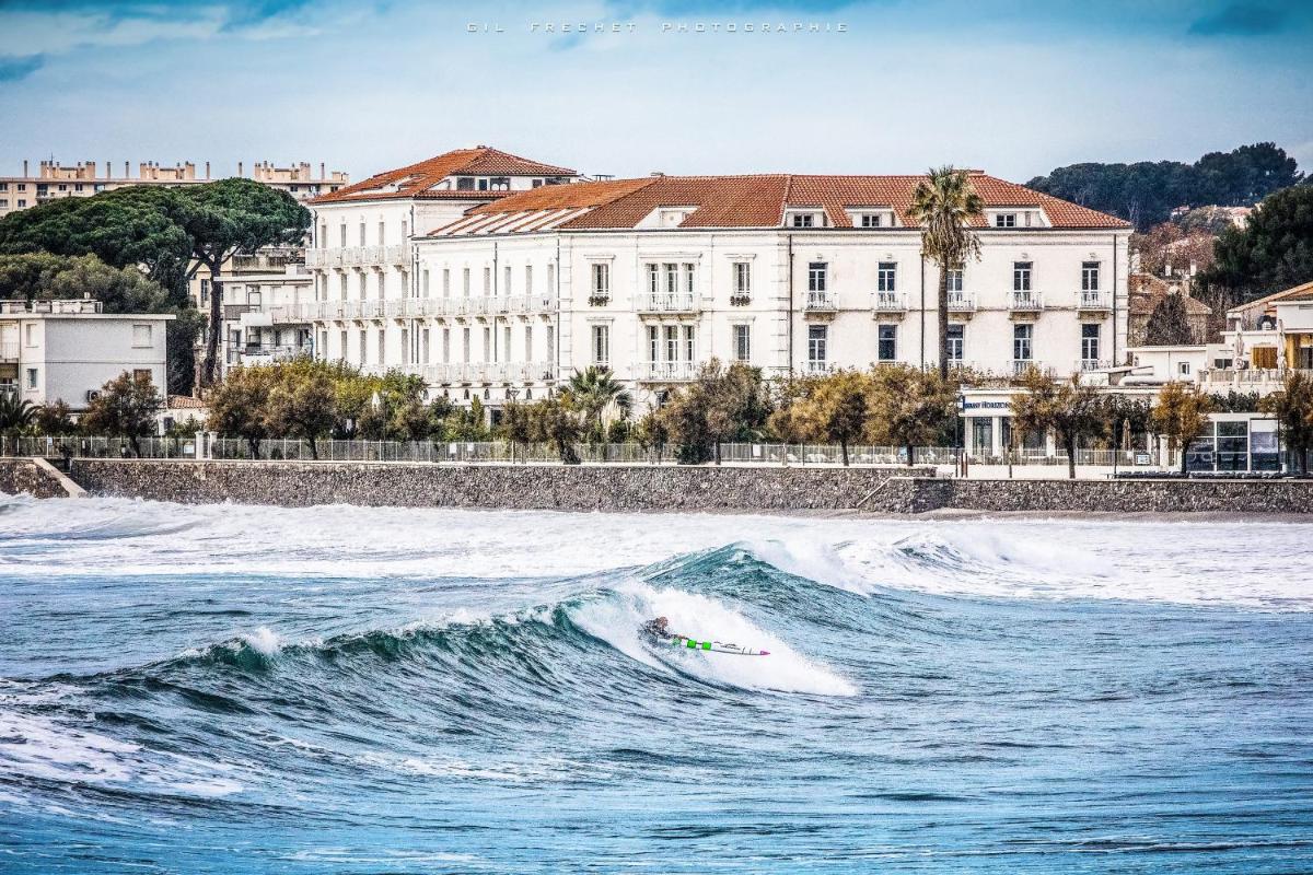 un surfeur fait une vague dans l'océan dans l'établissement Grand Hotel Des Sablettes Plage, Curio Collection By Hilton, à La Seyne-sur-Mer