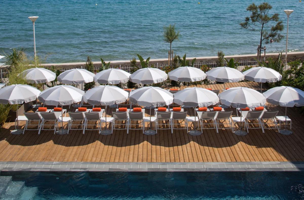 un groupe de tables et de chaises avec des parasols au bord d'une piscine dans l'établissement Grand Hotel Des Sablettes Plage, Curio Collection By Hilton, à La Seyne-sur-Mer