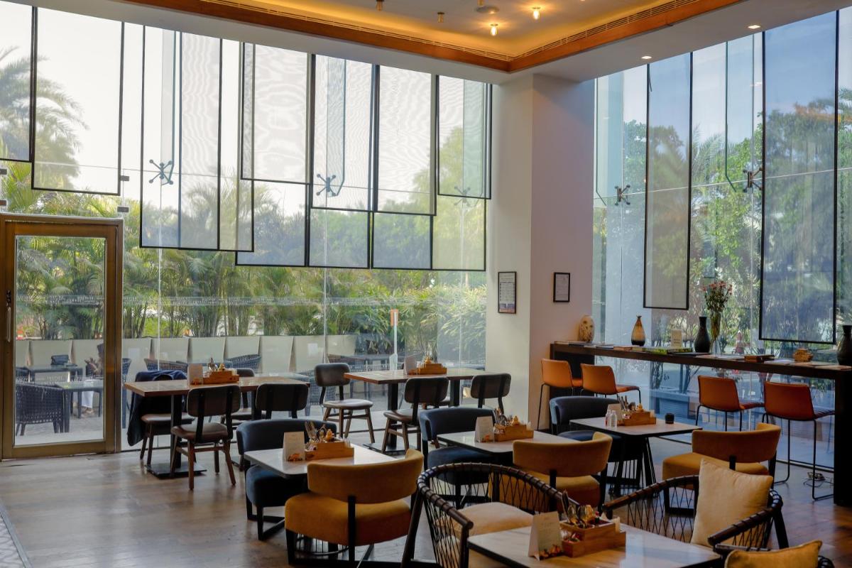 a restaurant with tables and chairs and large windows at Renaissance Ahmedabad Hotel in Ahmedabad