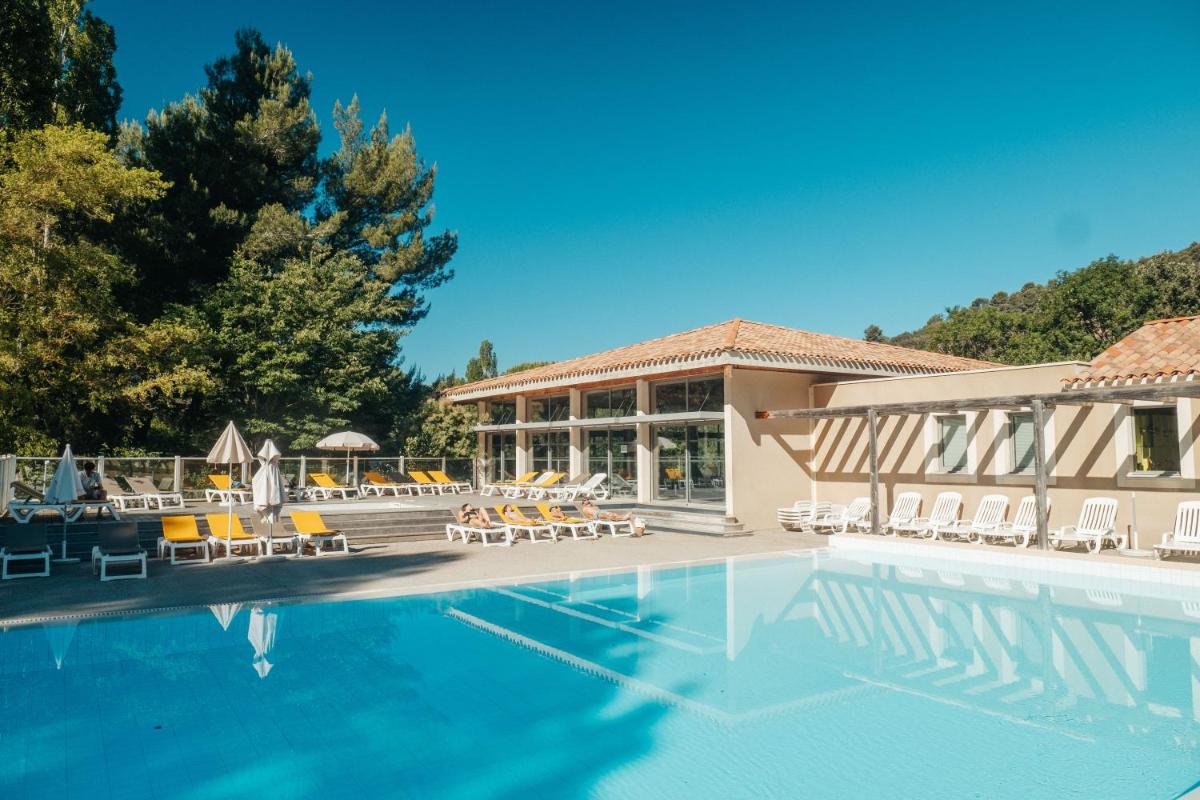 une piscine avec des chaises longues et un bâtiment dans l'établissement Club Vacances Bleues Domaine de Château Laval, à Gréoux-les-Bains