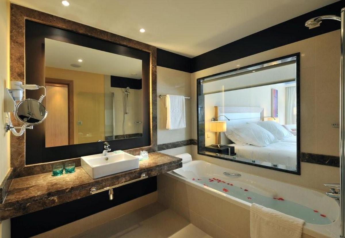 uma casa de banho com um espelho grande, uma banheira e uma cama em Pestana Promenade Ocean Resort Hotel no Funchal