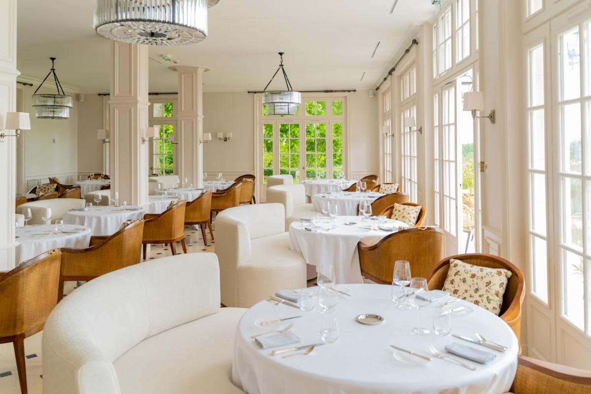 un restaurant avec des tables et des chaises blanches et des fenêtres dans l'établissement Château De Noirieux, à Briollay