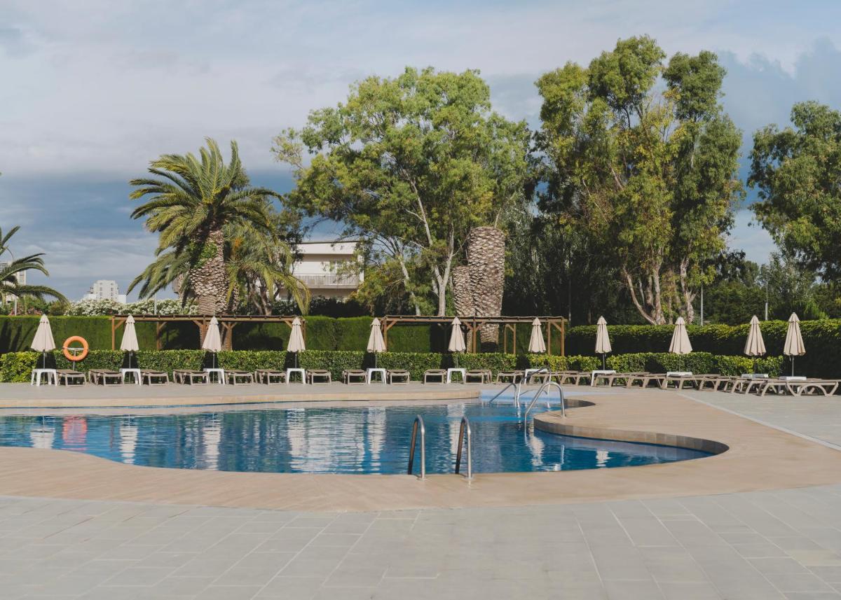 una piscina con sombrillas, sillas y árboles en Hotel Spa Mediterraneo Park, en Roses