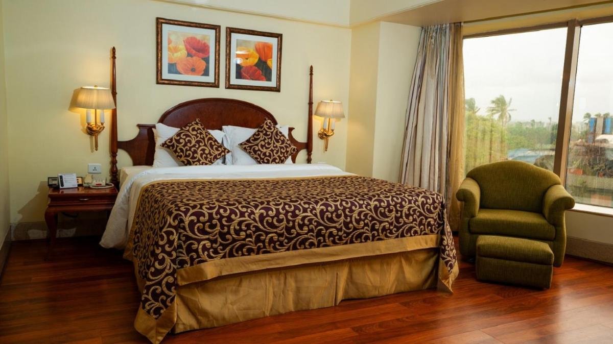 a bedroom with a bed and a chair and a window at Ramada Plaza By Wyndham Palm Grove in Mumbai
