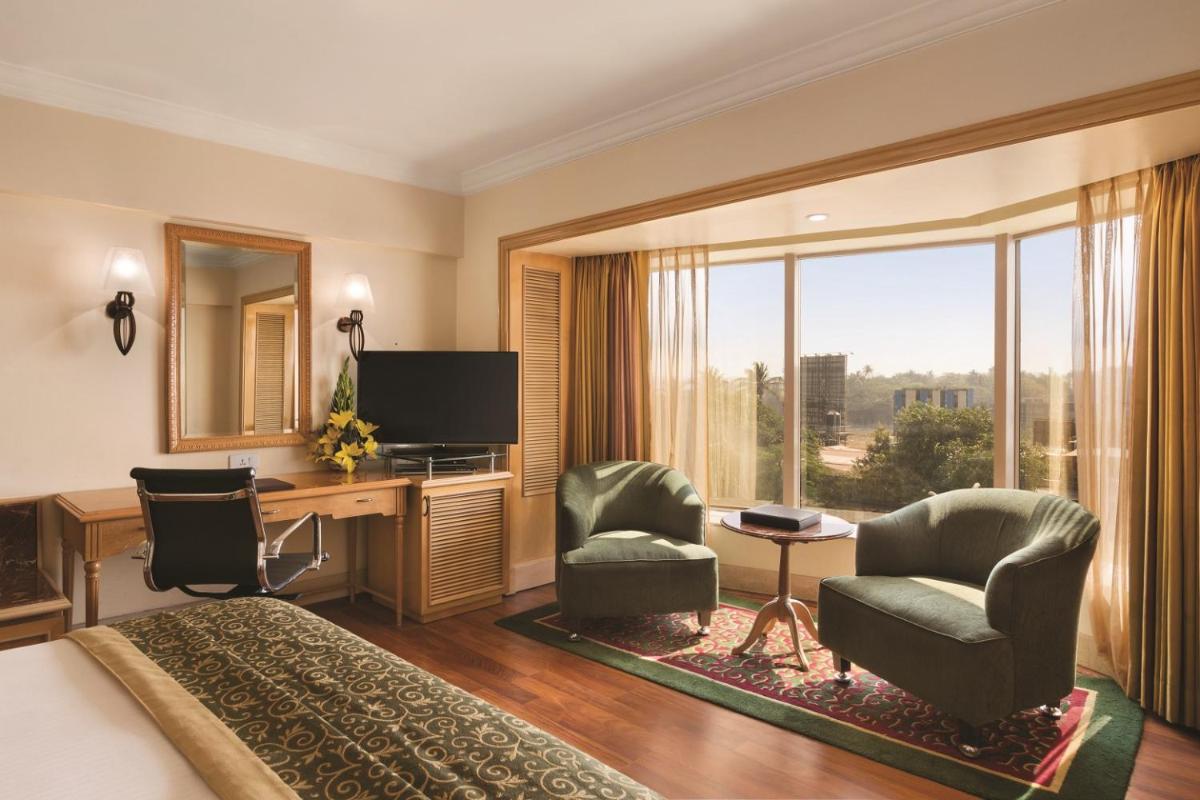 a hotel room with a bed and a desk and chairs at Ramada Plaza By Wyndham Palm Grove in Mumbai