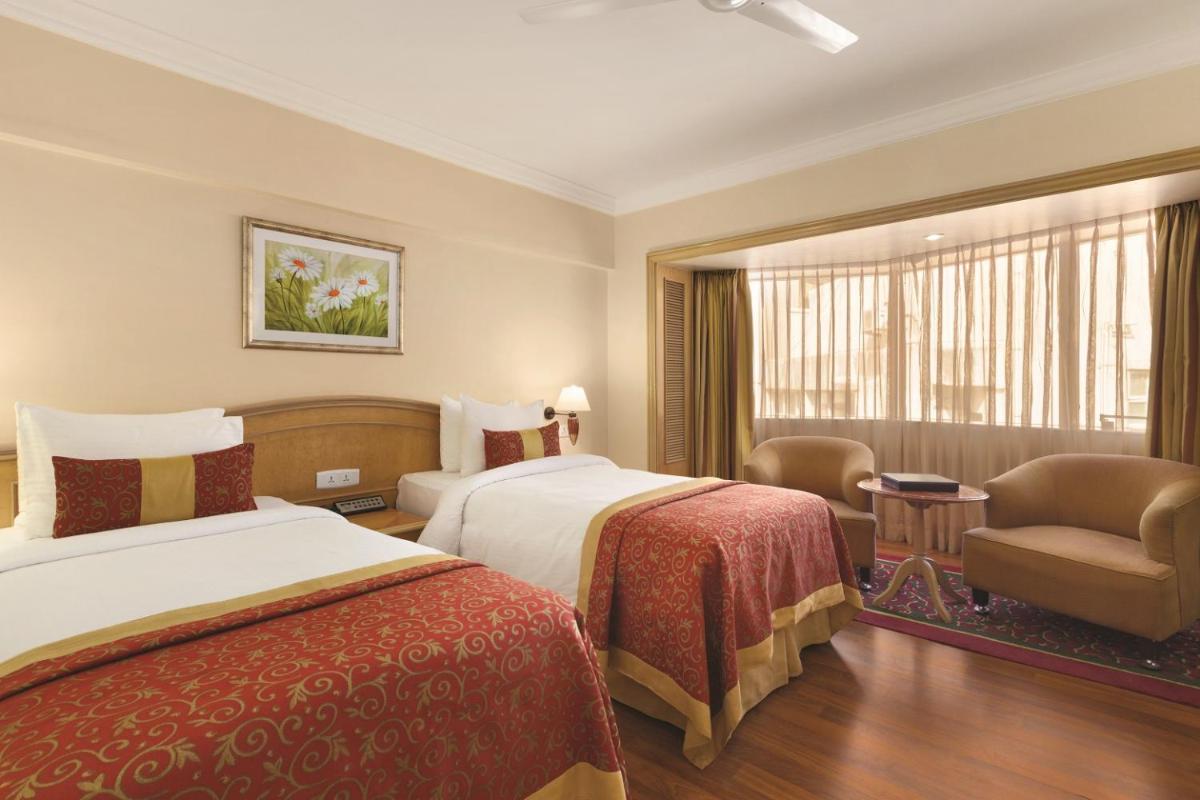 a hotel room with two beds and a chair at Ramada Plaza By Wyndham Palm Grove in Mumbai