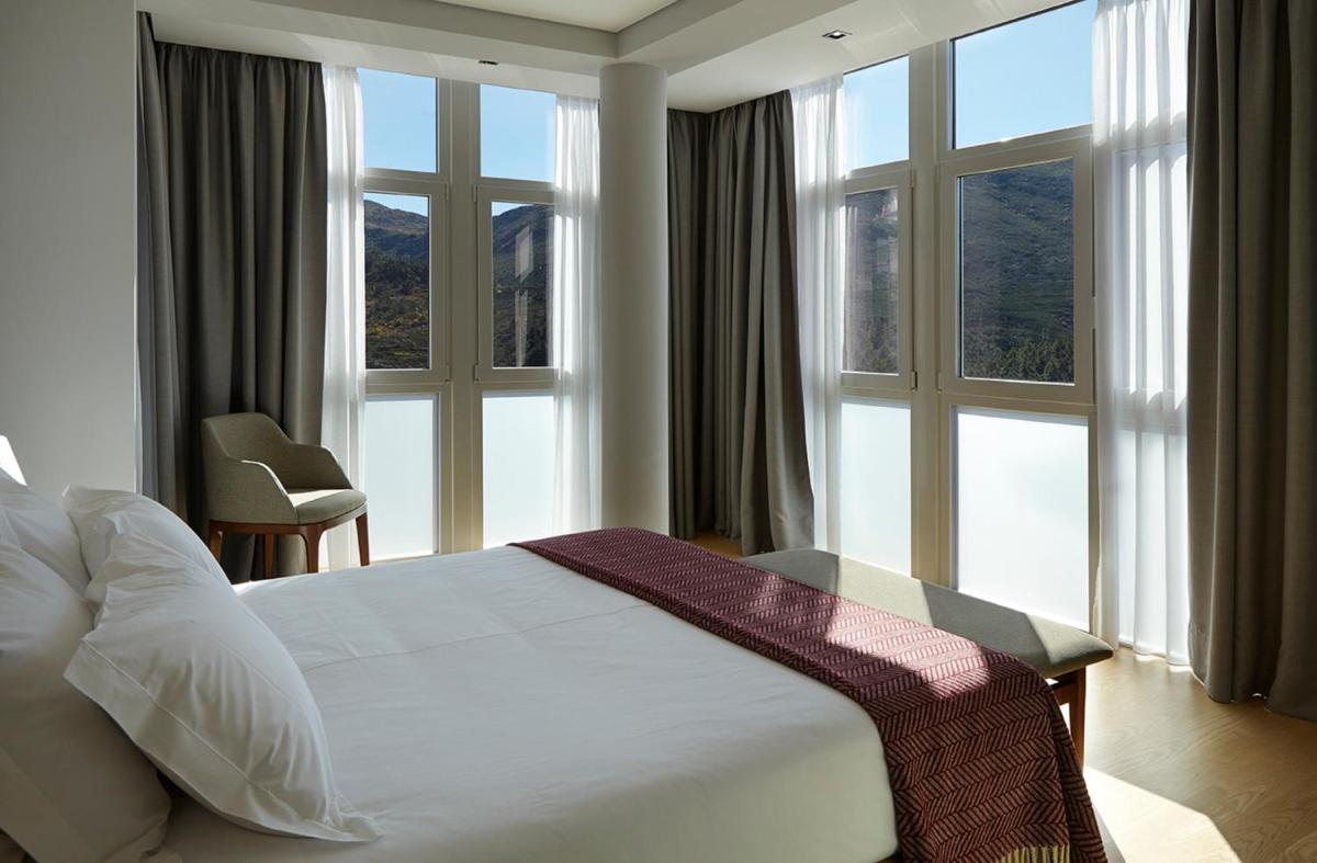 um quarto com uma cama branca e janelas grandes em Abrigo da Montanha Hotel Rural em Sabugueiro um quarto com uma cama branca e janelas grandes em Abrigo da Montanha Hotel Rural em Sabugueiro