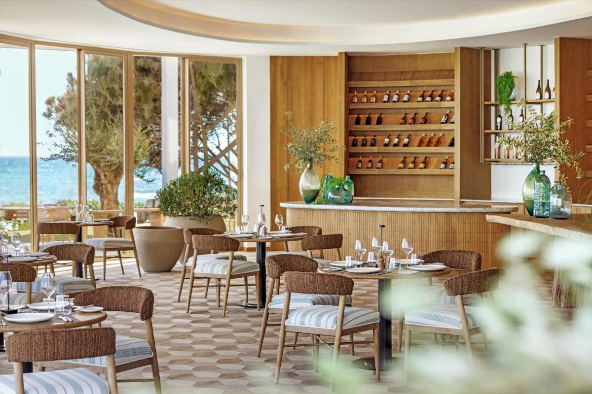 Un restaurante con mesas, sillas y ventanas. en Ikos Andalusia, en Estepona
