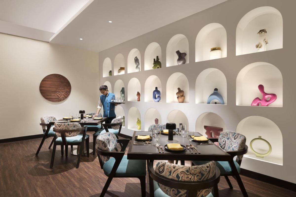 a woman standing in a dining room with tables and chairs at Novotel Kolkata Hotel and Residences in Kolkata a woman standing in a dining room with tables and chairs at Novotel Kolkata Hotel and Residences in Kolkata