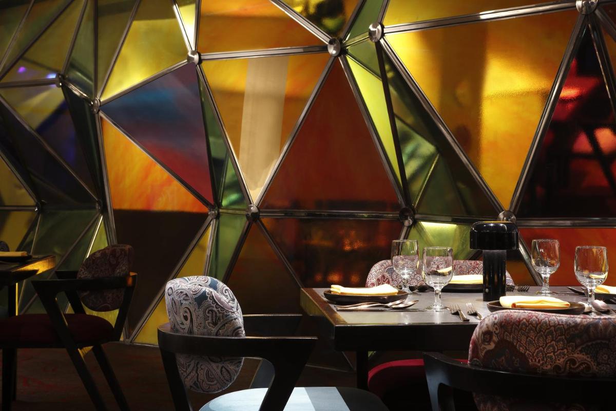a restaurant with a table and chairs and a geometric wall at Novotel Kolkata Hotel and Residences in Kolkata a restaurant with a table and chairs and a geometric wall at Novotel Kolkata Hotel and Residences in Kolkata