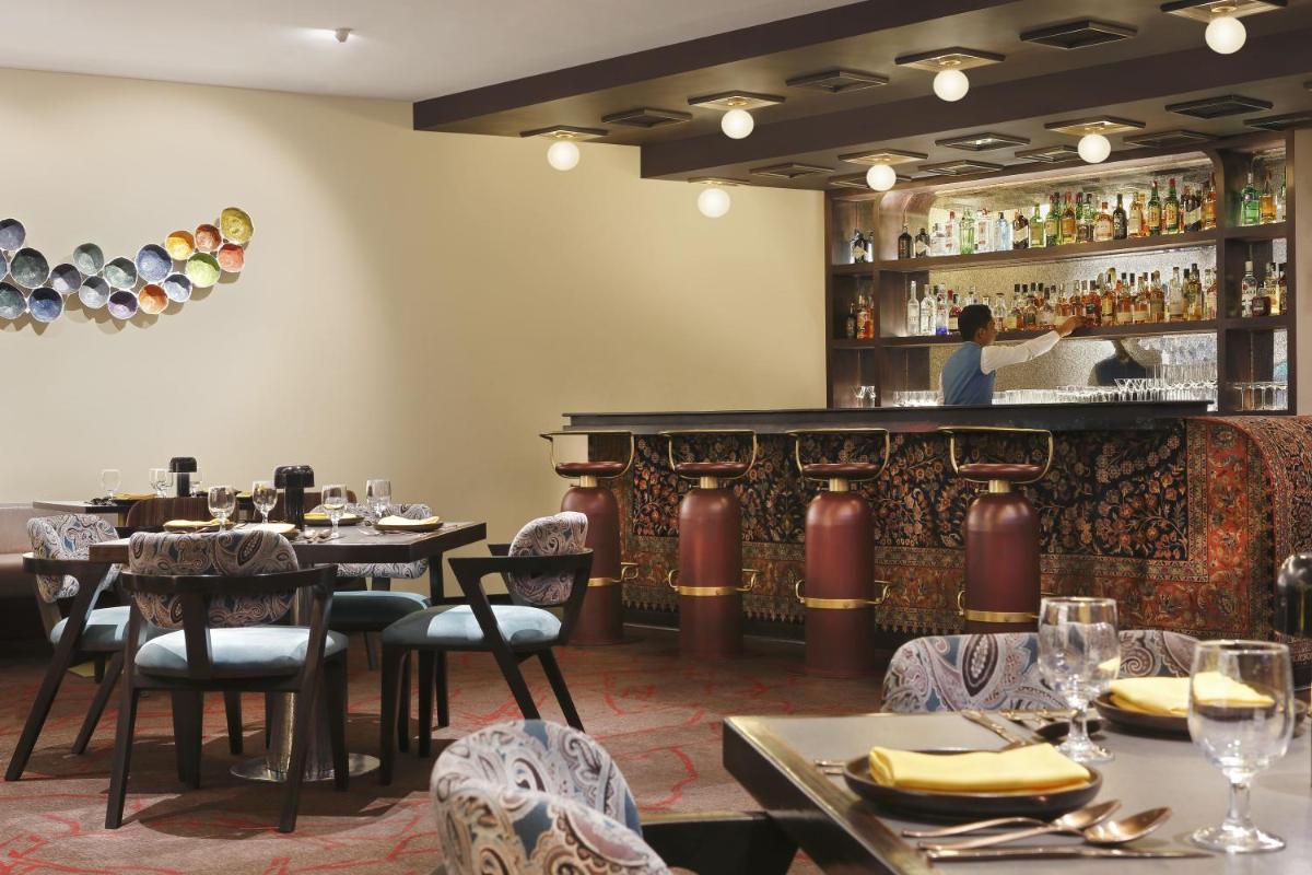 a restaurant with tables and chairs and a bar at Novotel Kolkata Hotel and Residences in Kolkata a restaurant with tables and chairs and a bar at Novotel Kolkata Hotel and Residences in Kolkata