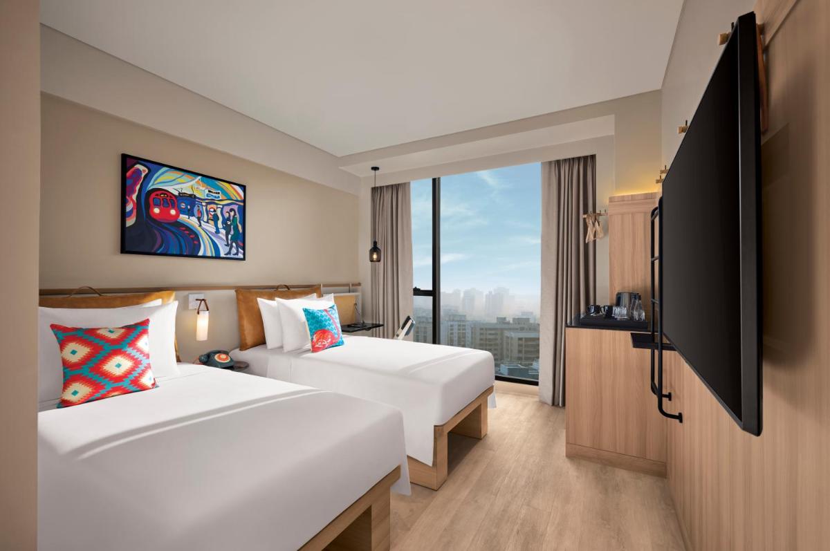 a hotel room with two beds and a large window at Moxy Mumbai Andheri West in Mumbai