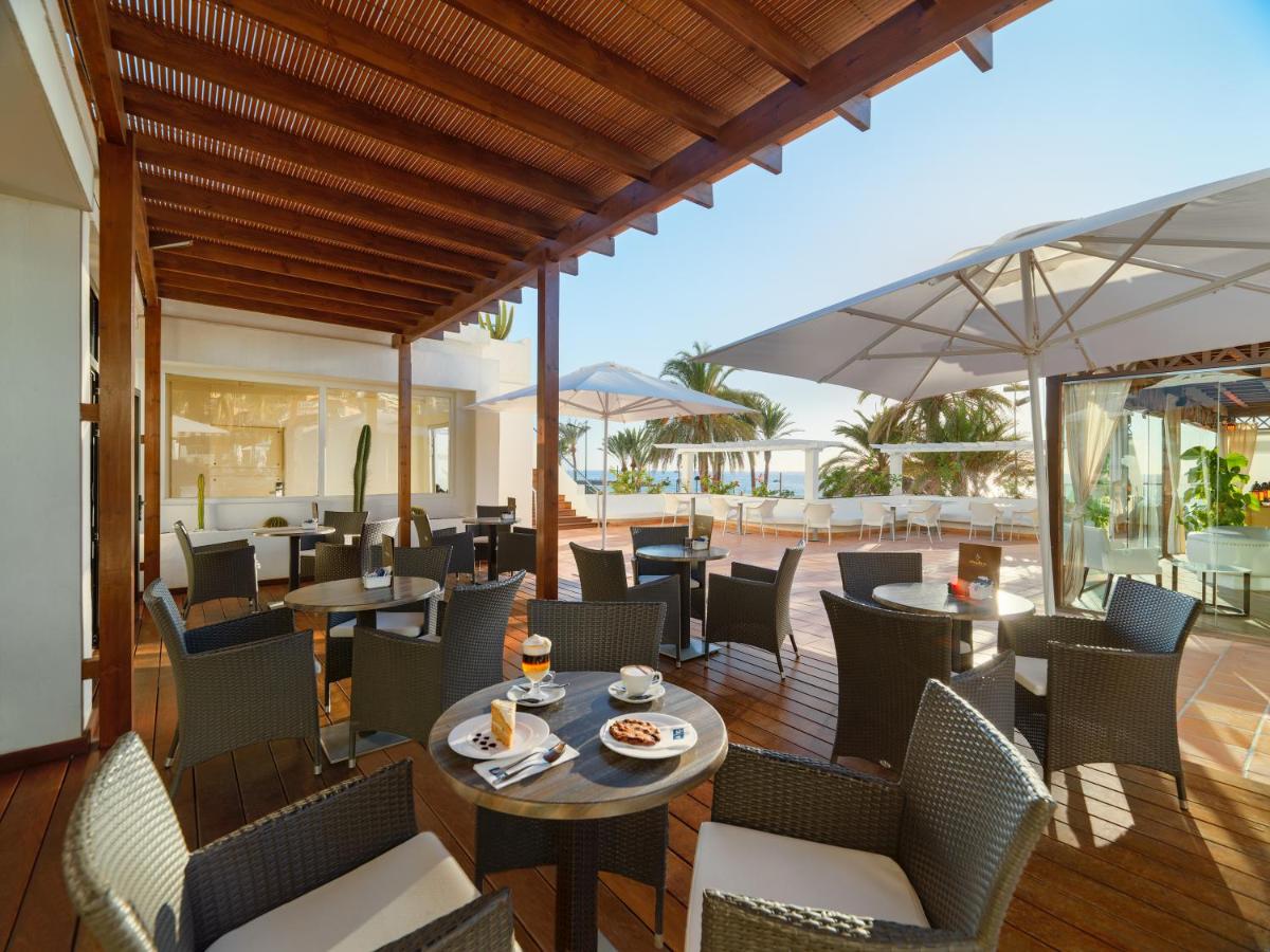 Un restaurante con mesas y sillas y una sombrilla. en H10 Gran Tinerfe - Adults Only, en Adeje