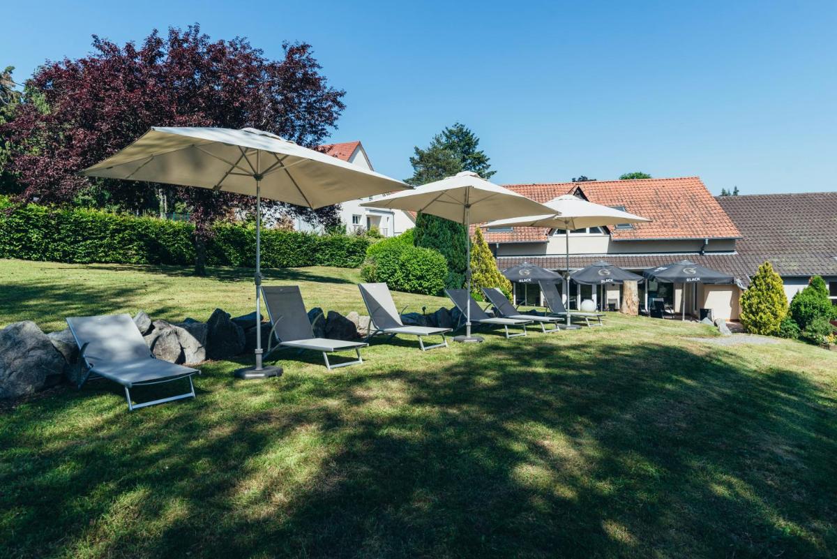 un groupe de chaises et de parasols dans une cour dans l'établissement Hotel Spa et Restaurant Au Chasseur, à Birkenwald