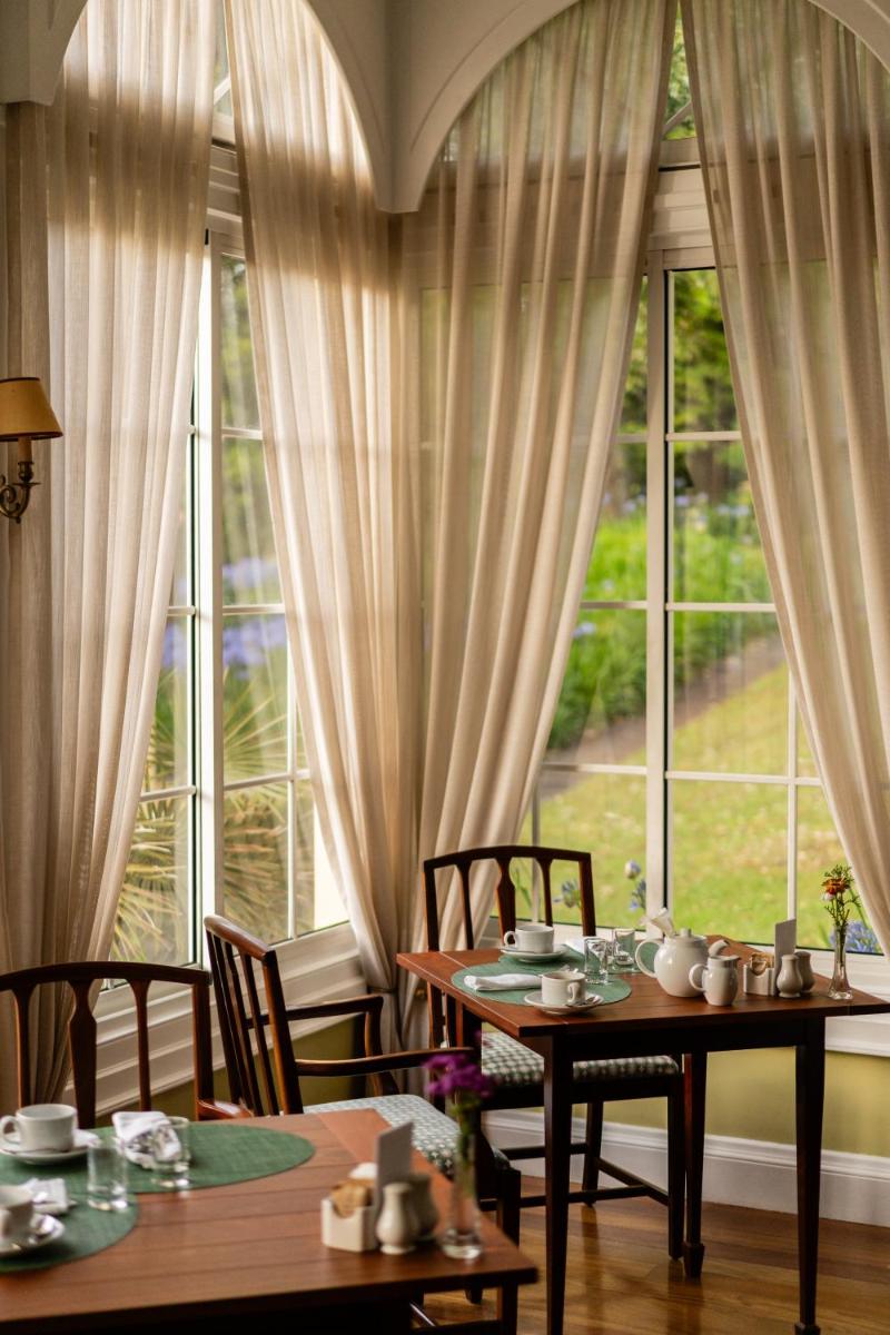 uma sala de jantar com duas mesas e uma grande janela em Casa Velha do Palheiro Relais & Chateaux no Funchal