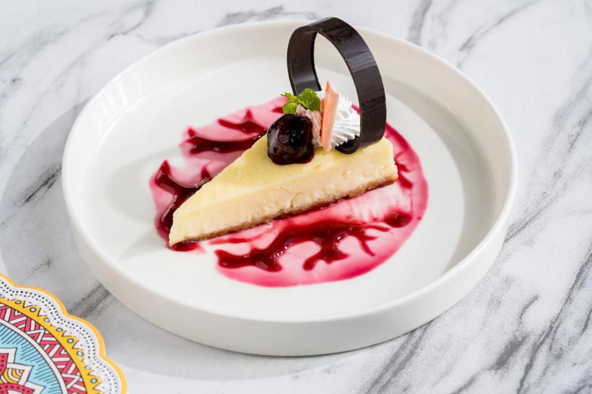 a piece of cheesecake on a white plate with red sauce at Holiday Inn Lucknow Airport by IHG in Lucknow