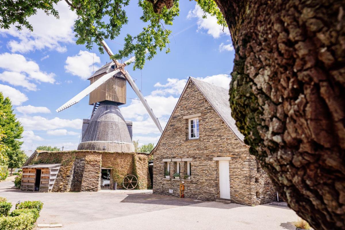 un vieux moulin avec un moulin à vent au sommet dans l'établissement Logis Hôtel Domaine du Moulin Cavier - Restaurants & Spa, à Avrillé