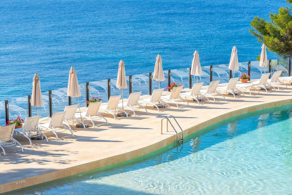 Una piscina con sillas y sombrillas junto al mar. en Park Hotel San Jorge & Spa by Escampa Hotels, en Platja d'Aro